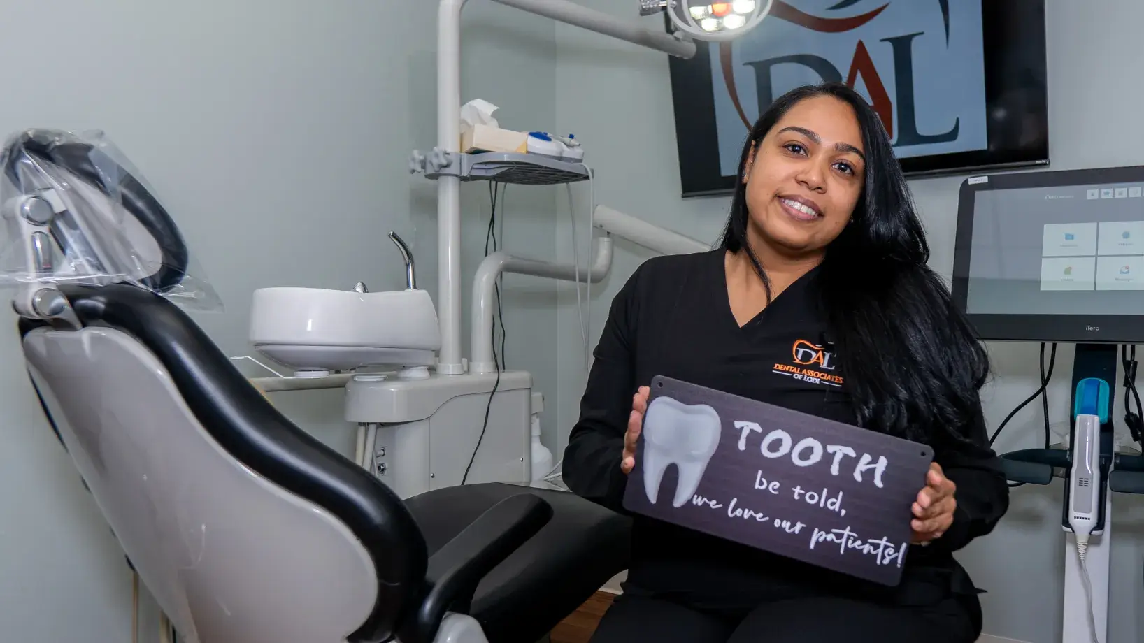 A dentist sits in a treatment room holding a sign about patient care.