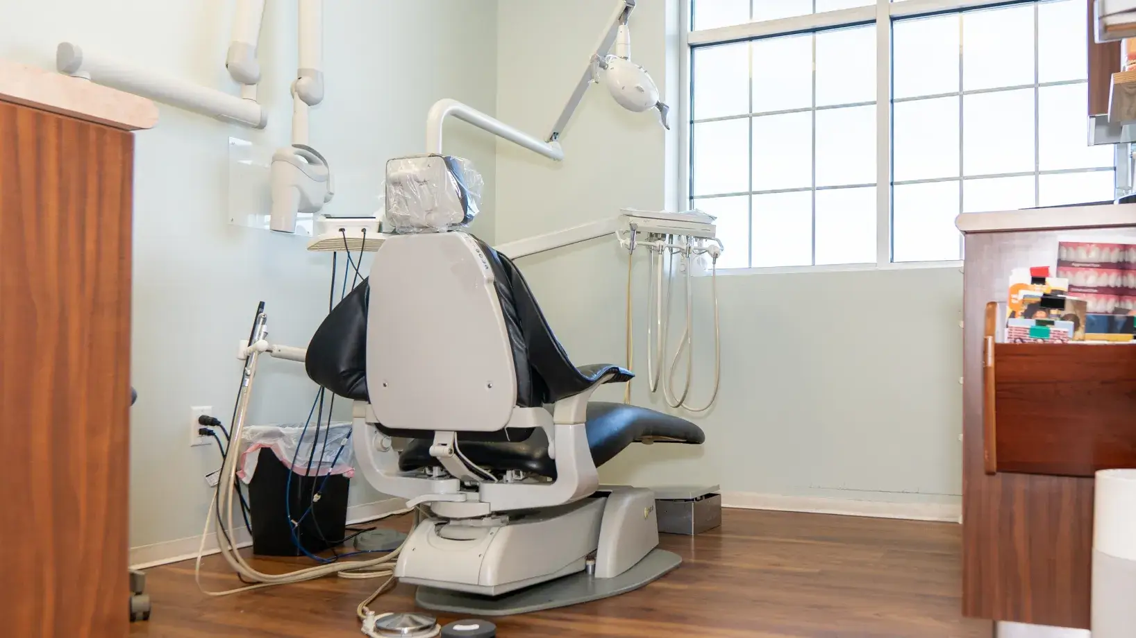 Empty dental chair in a bright room with dental equipment and a large window.