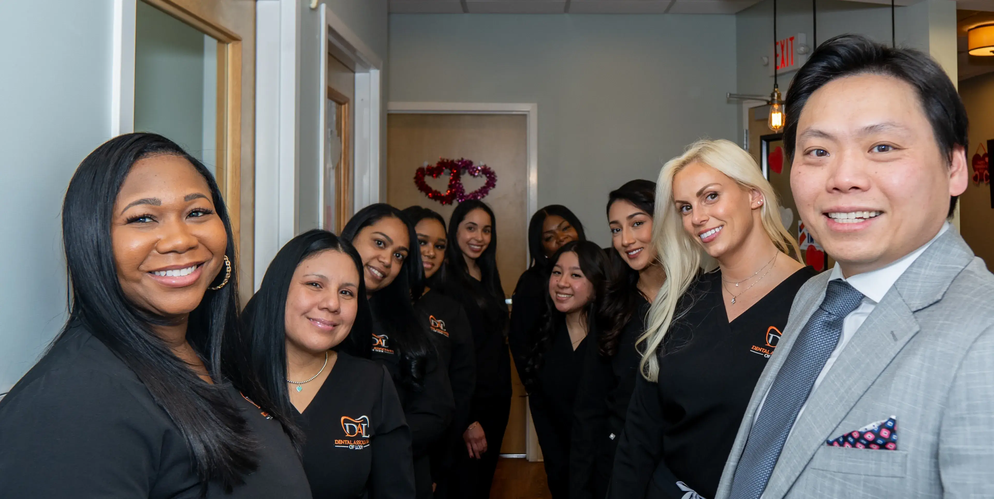 A group of people in matching black uniforms smile in a hallway, with a man wearing a suit.