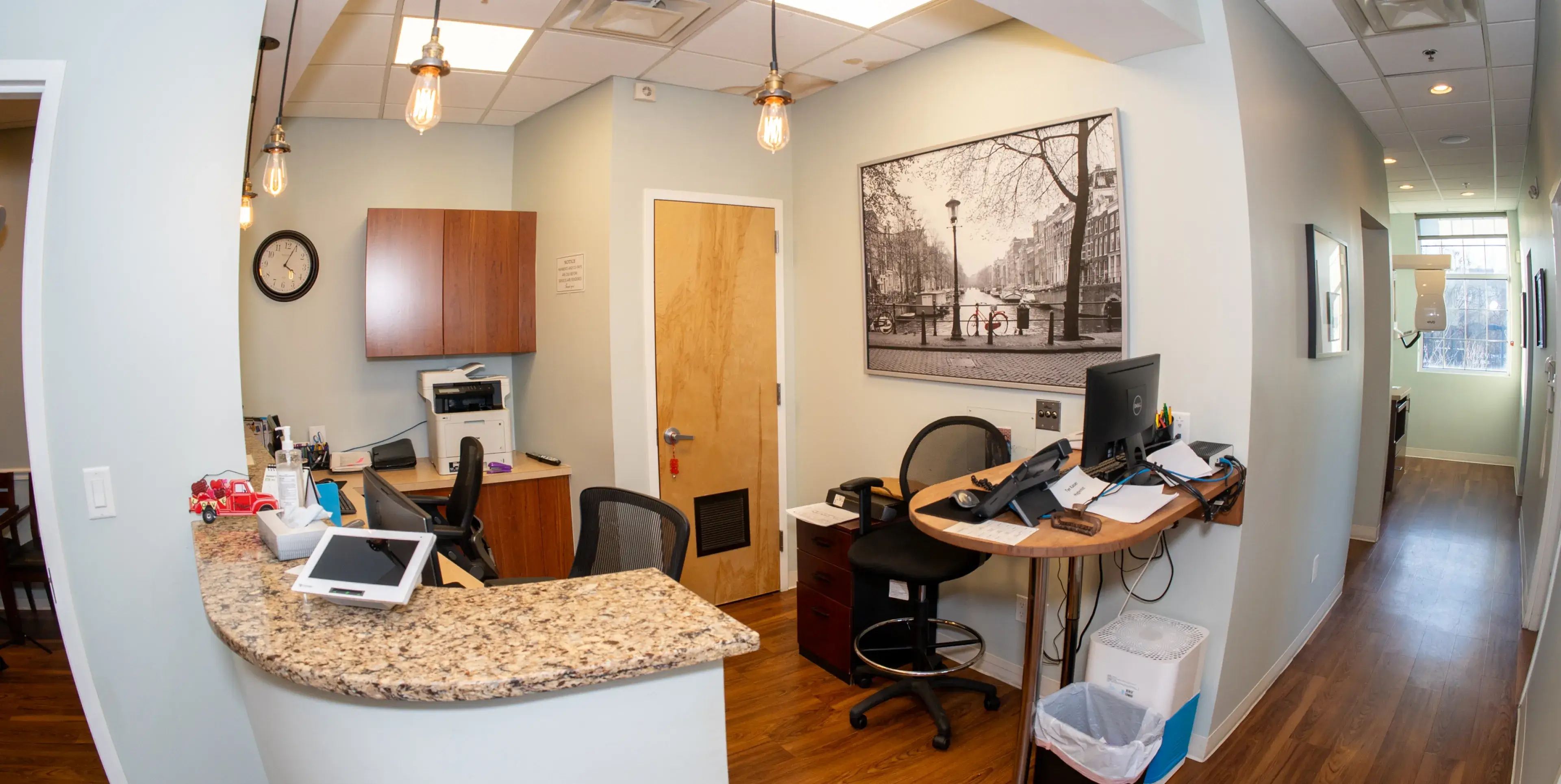 A small reception area with a curved granite desk, computer, and printer near a closed door.