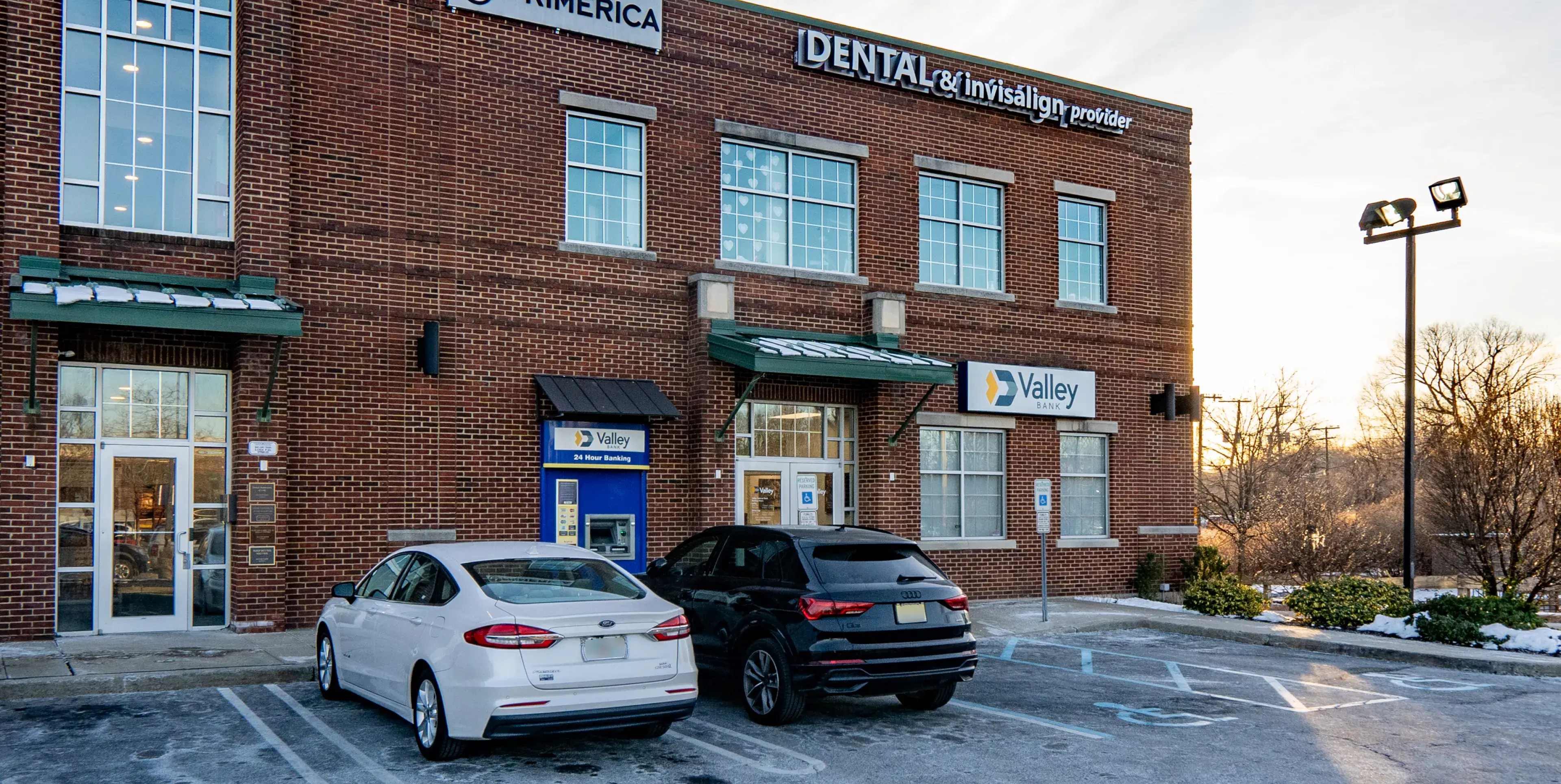 Two cars parked in front of a brick building housing Valley Bank with an ATM and a dental and Invisalign provider office.