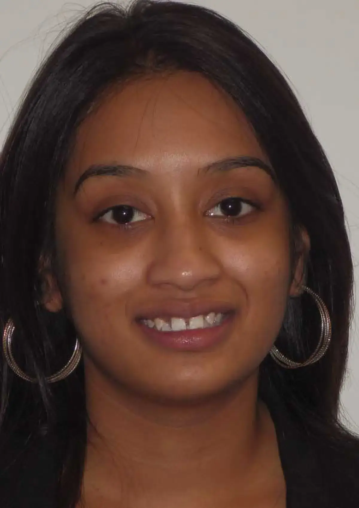 A person with long dark hair and hoop earrings is smiling in a close-up photo.