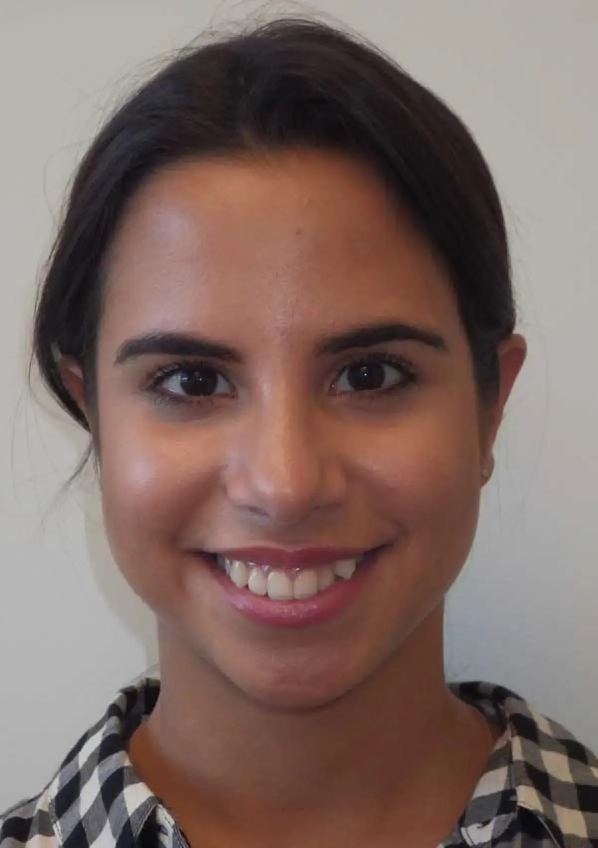 Smiling woman with dark hair wearing a checkered shirt, looking directly at the camera.