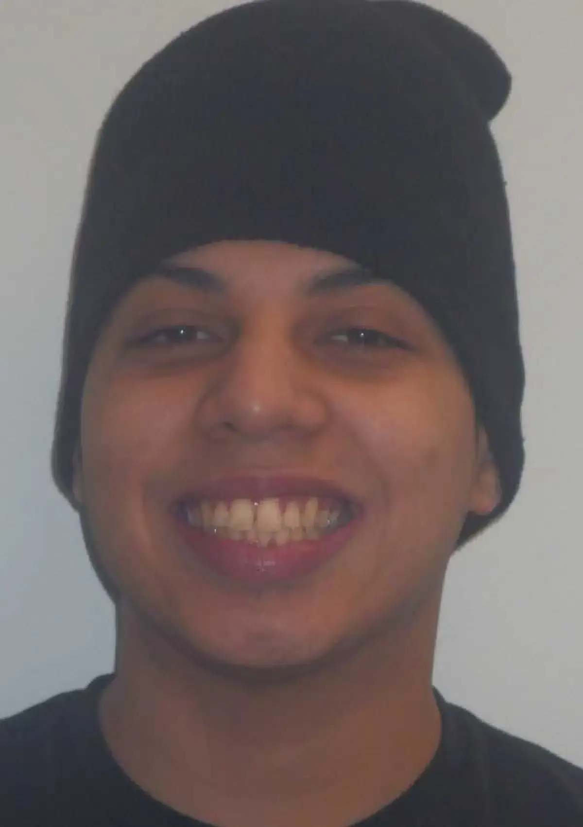 Person smiling, wearing a black beanie and a dark shirt, against a plain background.