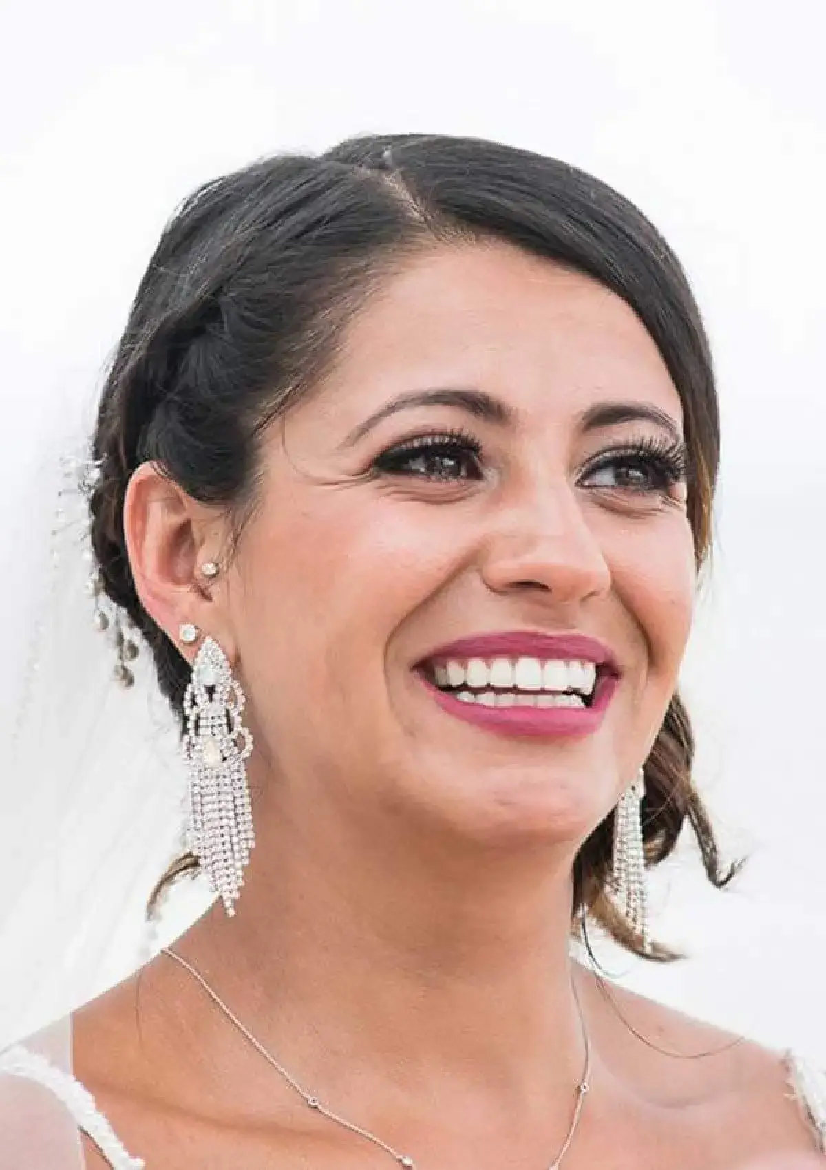 A woman with braided dark hair is smiling broadly, wearing large, dangling earrings.