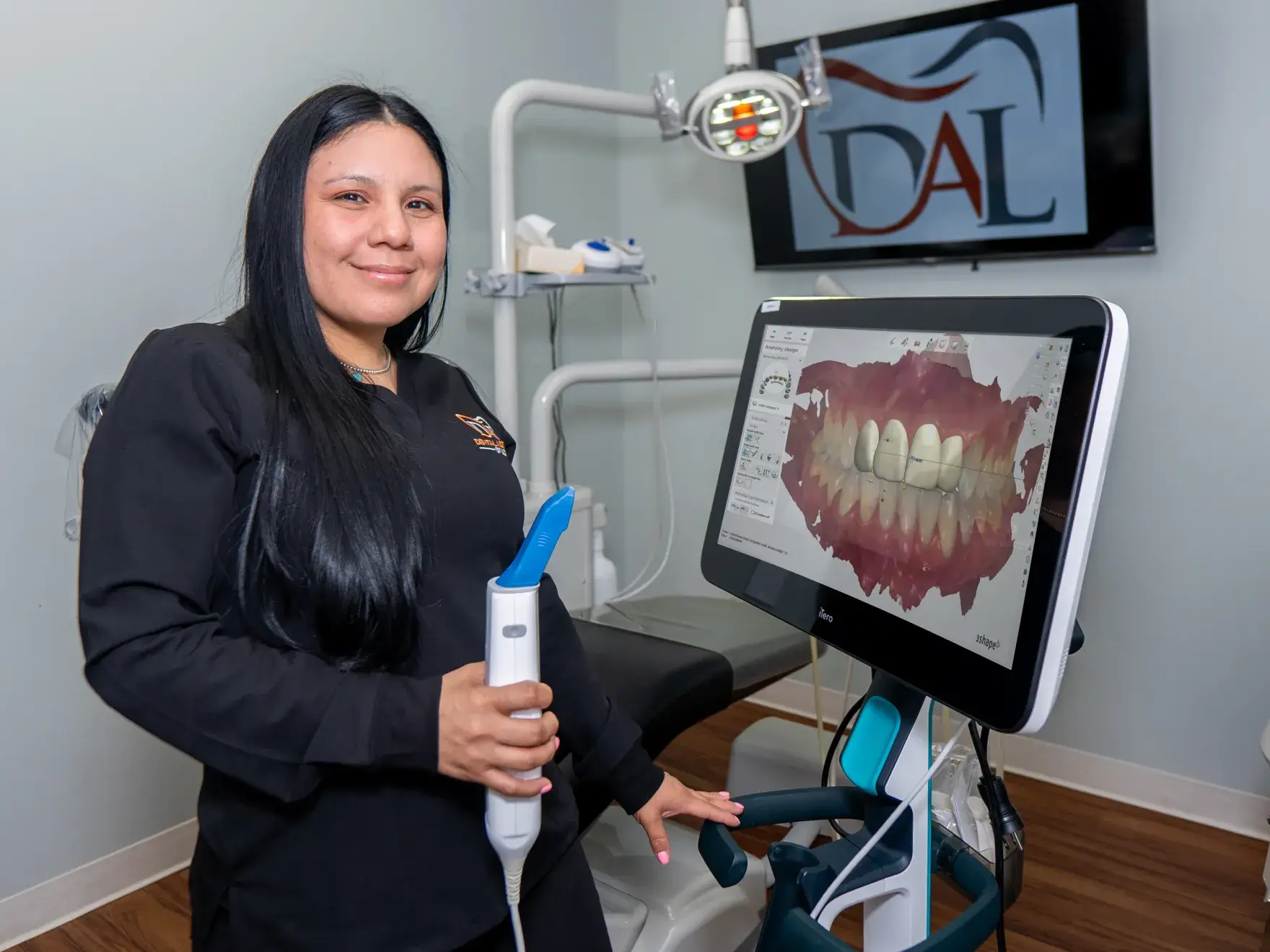 A dental assistant stands by a digital imaging machine displaying a 3D model of teeth.