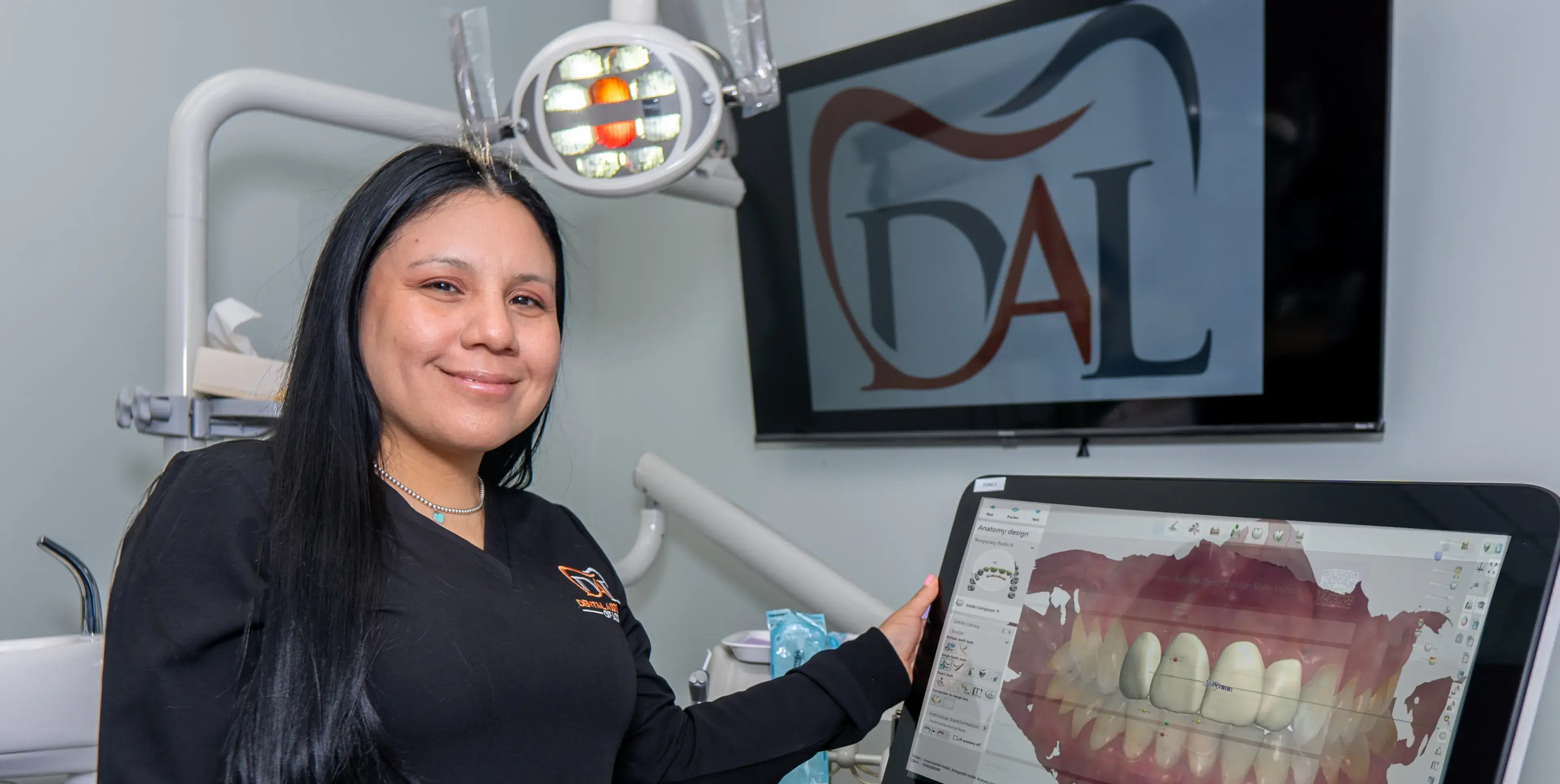 A woman in a dental office smiles while holding a screen displaying digital teeth images.