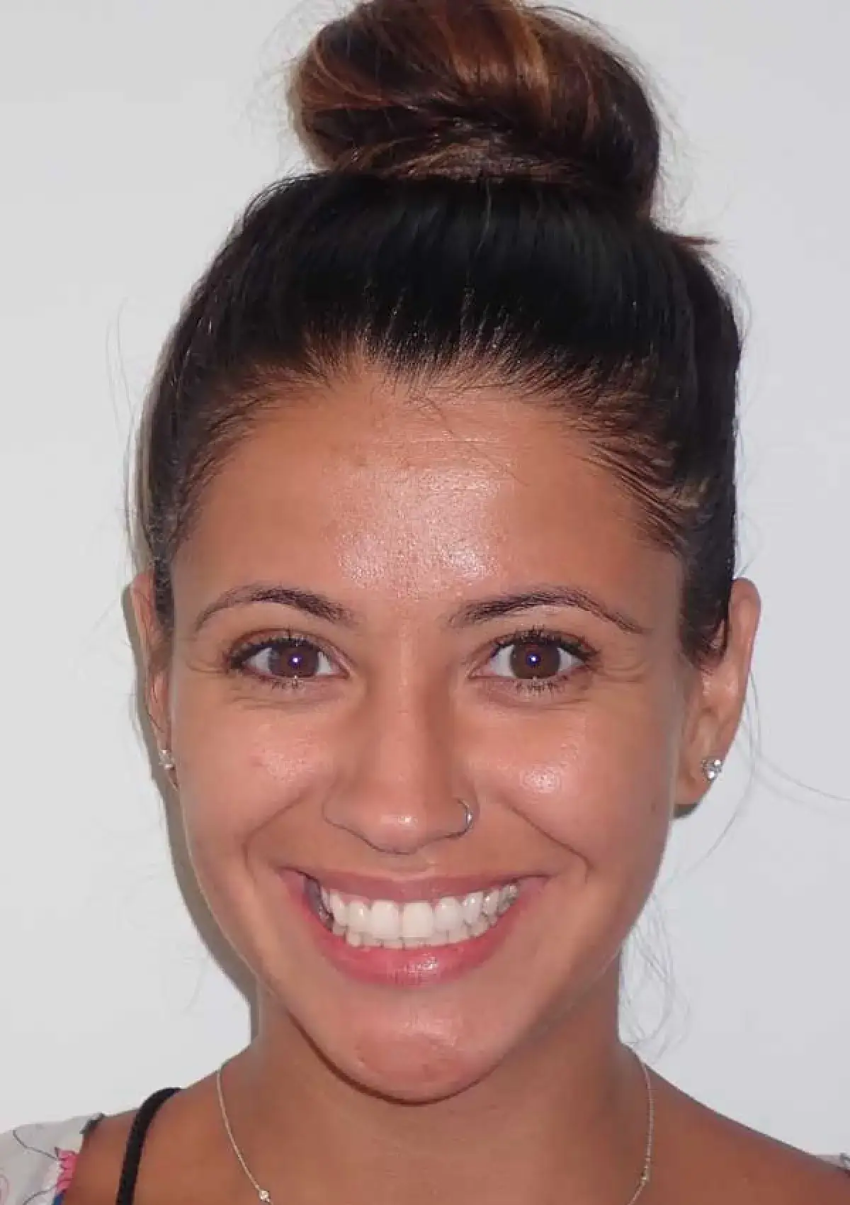 A person is smiling at the camera with their hair in a bun.