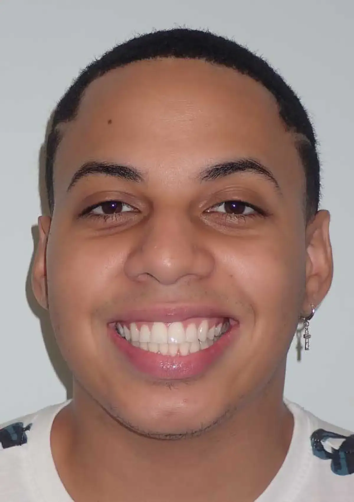 A person smiling directly at the camera, wearing a white shirt and an earring.