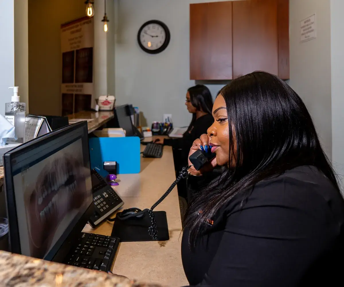 A woman is speaking on the phone while looking at dental X-rays on a computer screen.