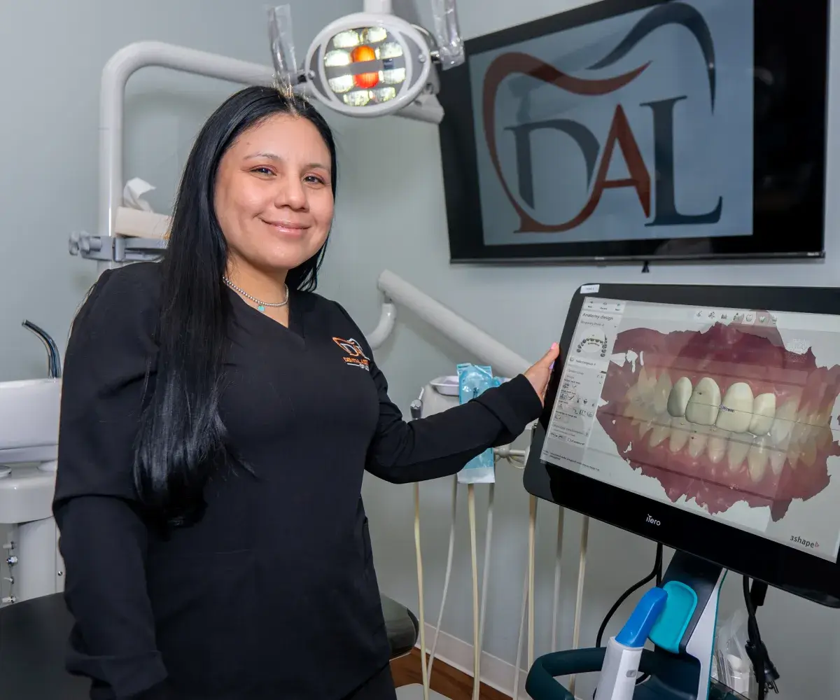 A dental professional stands smiling beside a computer display showing a dental image in a clinic.