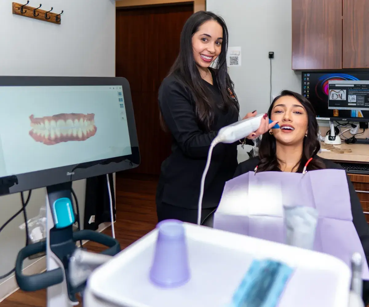 A dental professional uses a scanner on a patient's teeth, with a digital display showing results.