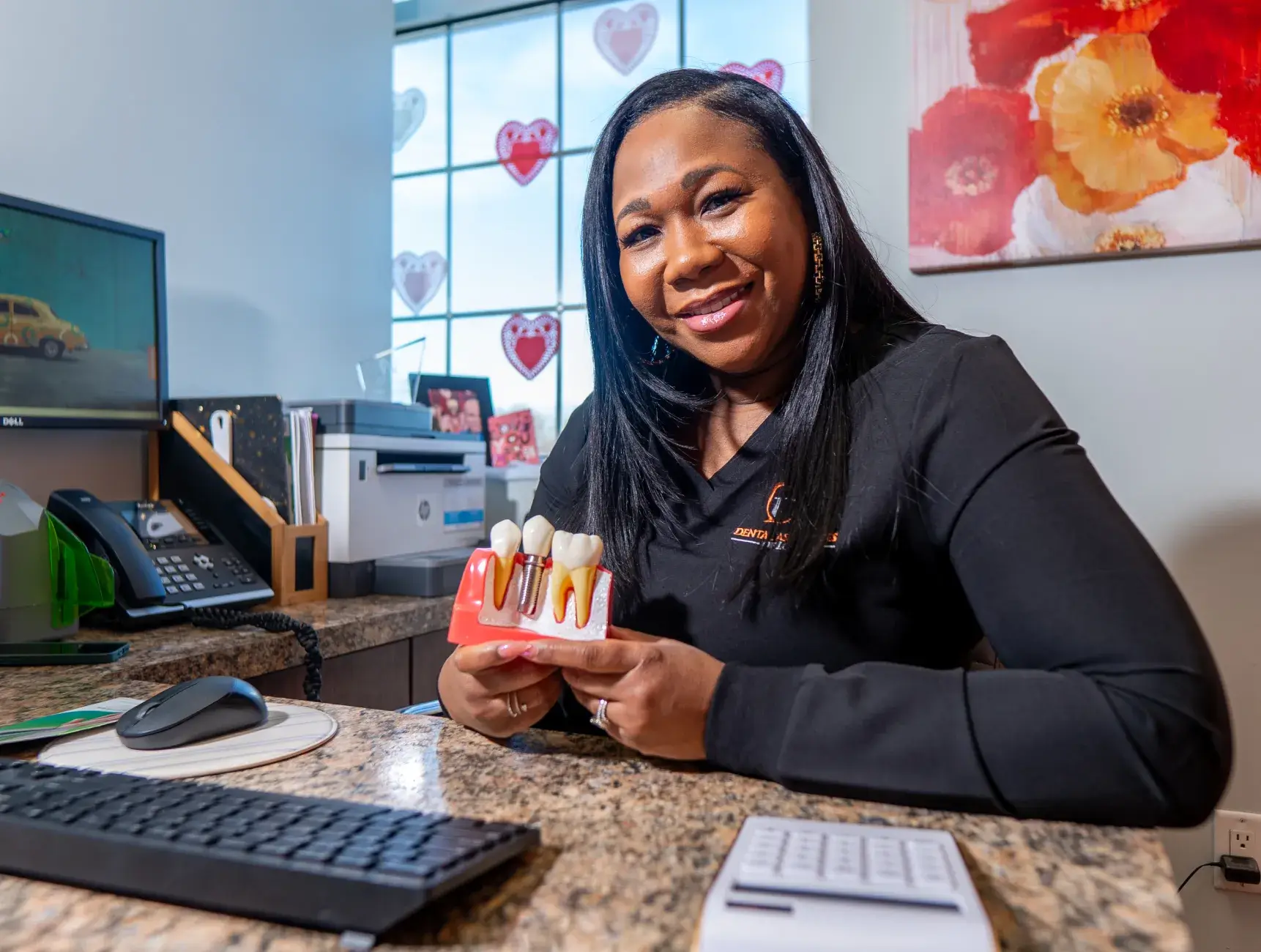 A woman in an office smiles while holding a dental model showing teeth and gums.