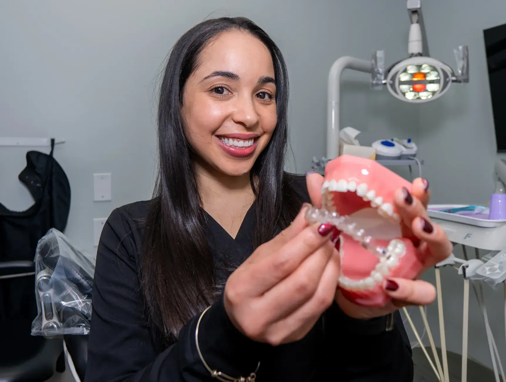 A dentist holds a dental model, demonstrating how to fit a clear aligner on teeth.