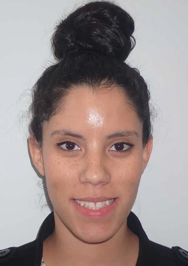A woman with dark hair in a bun smiles at the camera, wearing a dark jacket.