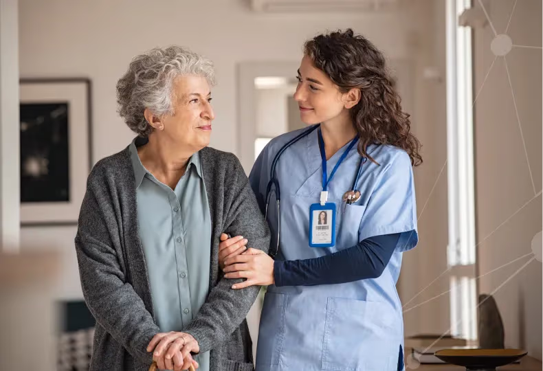 Nurse gently supporting elderly woman with a cane in a warm indoor setting.