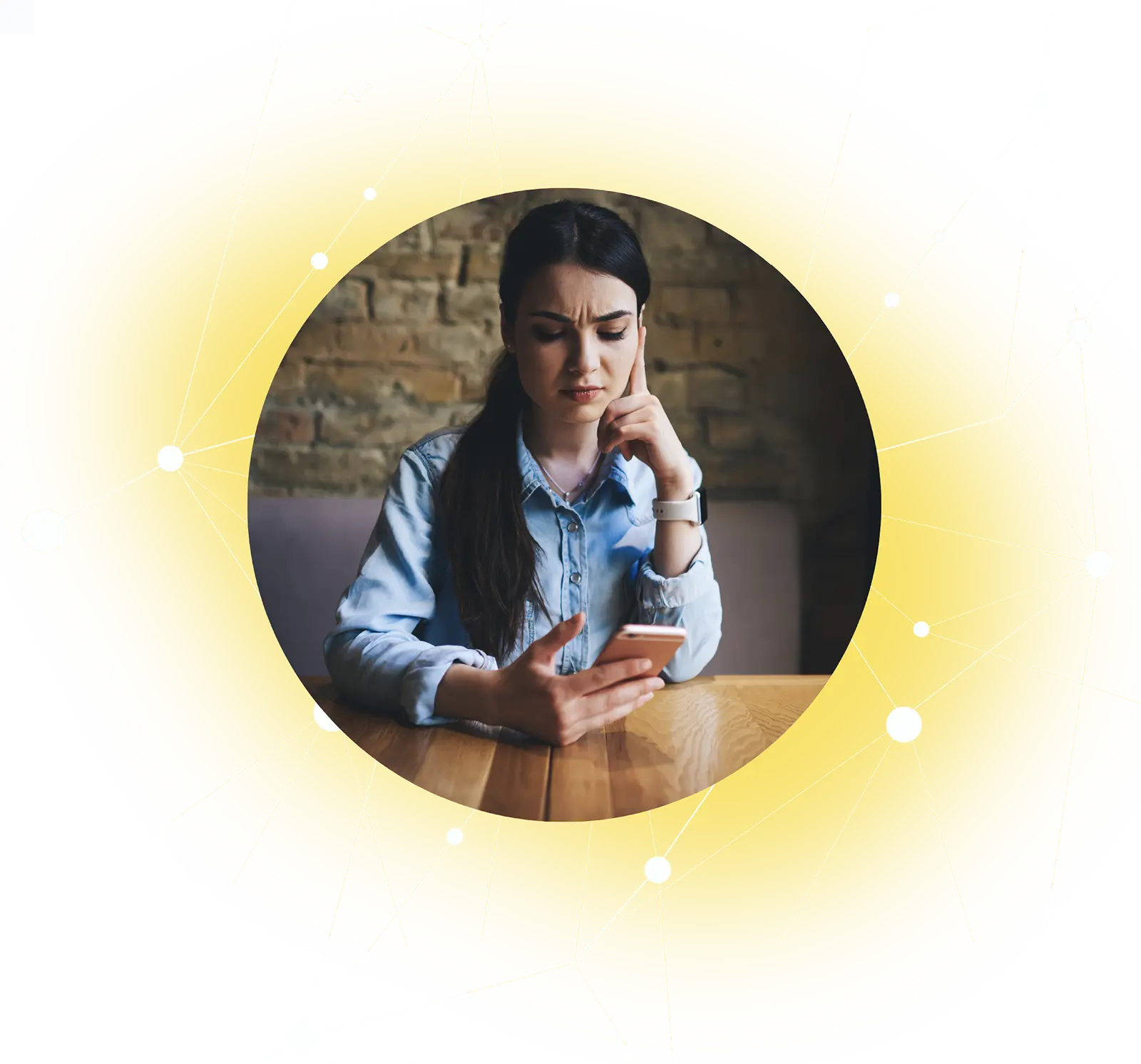 Woman in a denim shirt sitting at a table, looking worried while holding a smartphone.