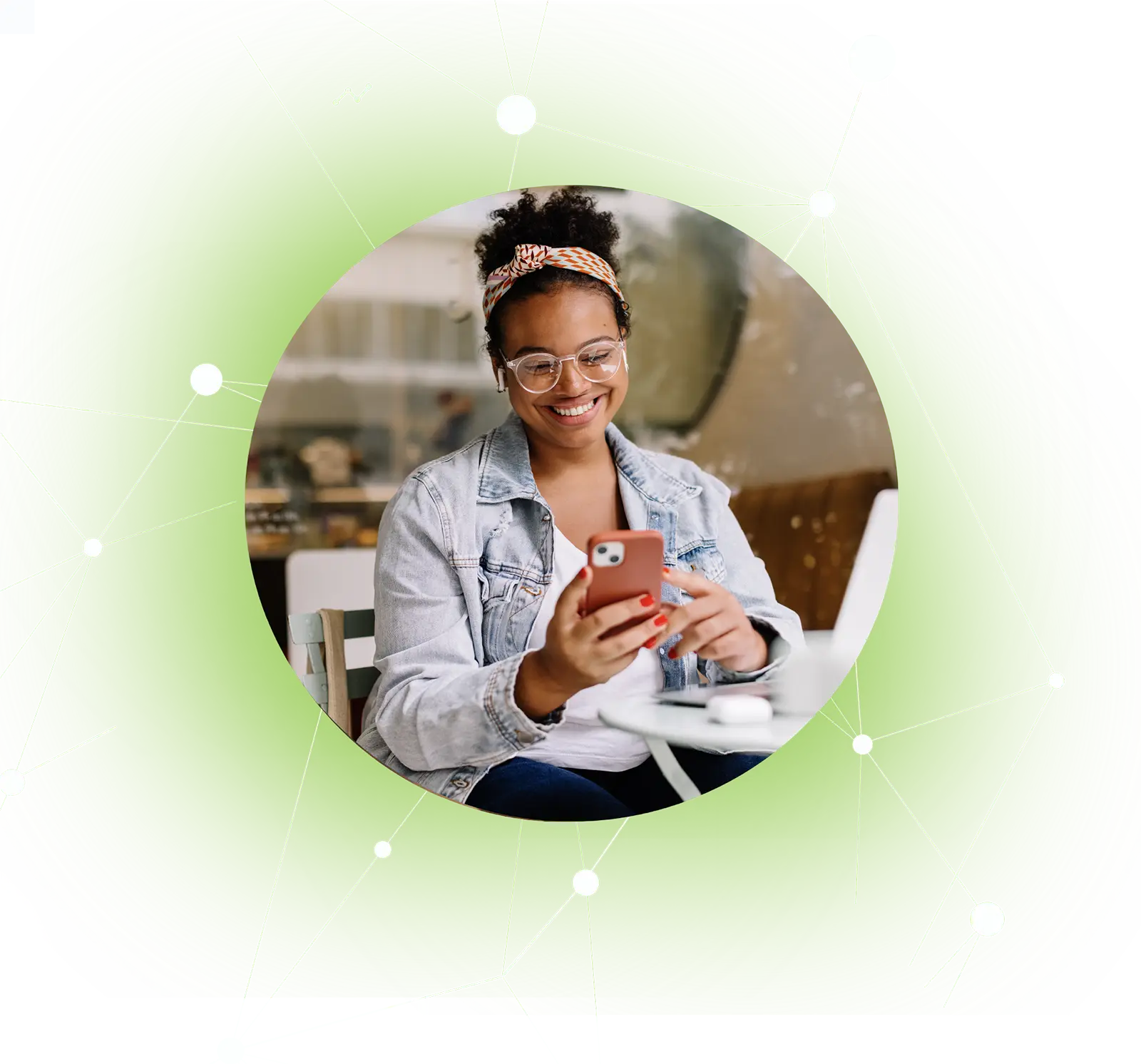 Smiling woman wearing glasses and headband uses smartphone at a café table.