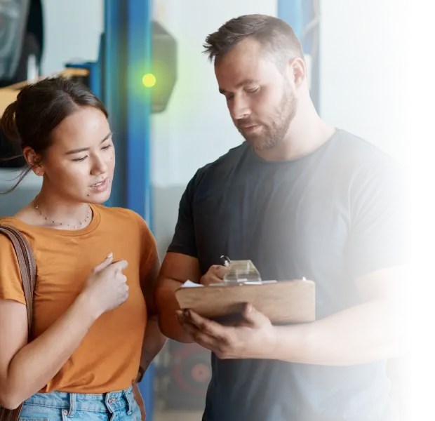 A man holding a clipboard discussing details with a woman in a casual setting.
