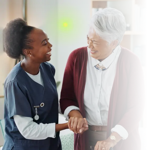 Smiling nurse holding hands with elderly woman in cozy home setting.