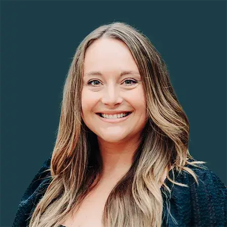 Smiling woman with long blonde hair wearing a black top against a dark background.