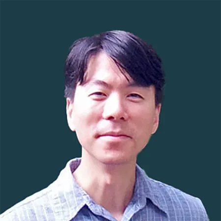 Portrait of a smiling man with black hair wearing a light blue checkered shirt against a dark background.