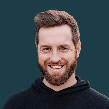Smiling man with brown hair and beard wearing a black hoodie against a teal background.