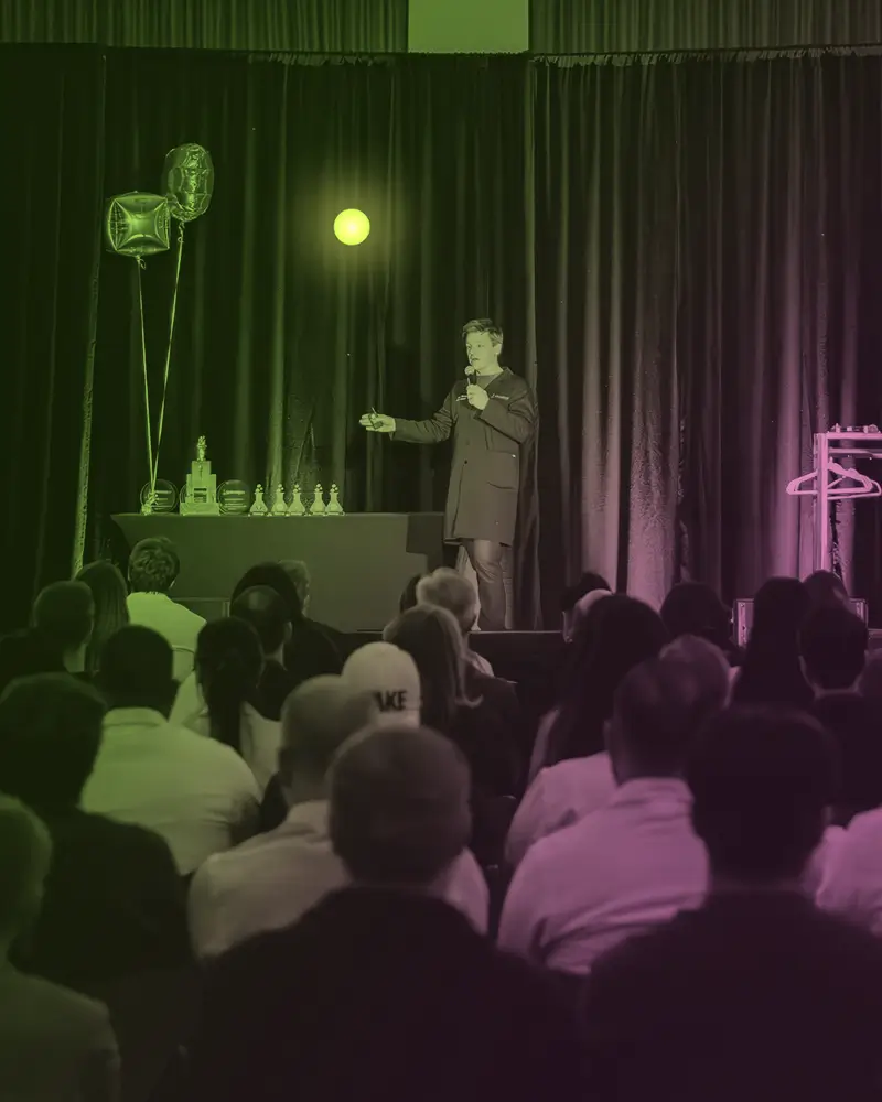 Speaker holding a microphone on stage presenting to an audience seated in rows.