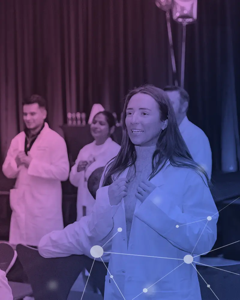 Young woman smiling and adjusting white lab coat with three people in lab coats behind her.