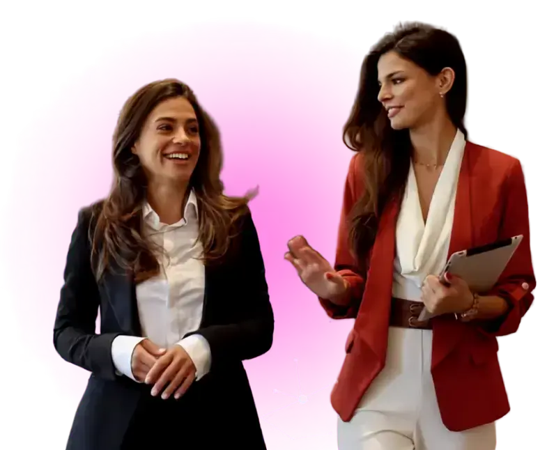 Two women in professional attire smiling and talking against a pink circular background.