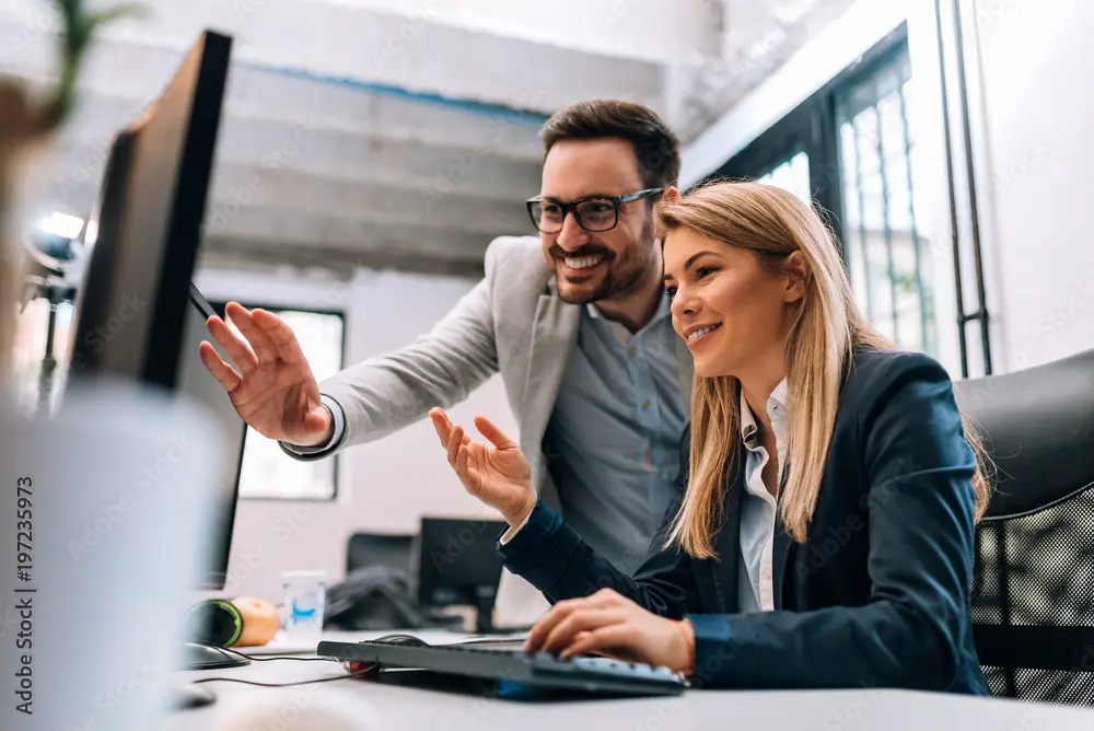 Man and woman smiling and working together at a computer in a modern office.