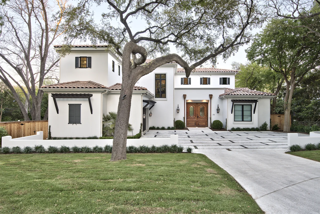 Front elevation in white stucco with a clay tile roof, framed by a live oak