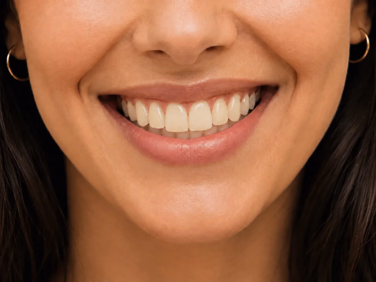 Close-up of a smiling woman showing her teeth and wearing small hoop earrings.