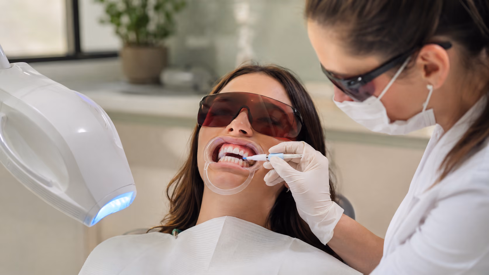 Dentist applies whitening gel to a woman's teeth during a professional teeth whitening treatment.