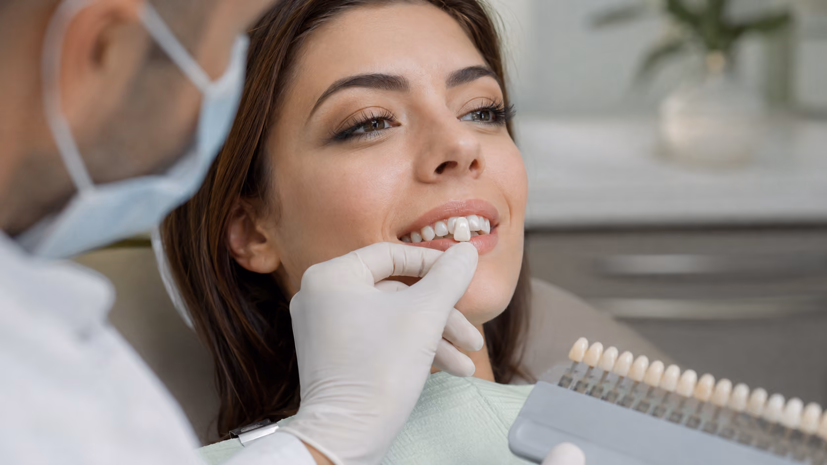 Dentist in gloves fitting a porcelain veneer on smiling woman's front teeth.