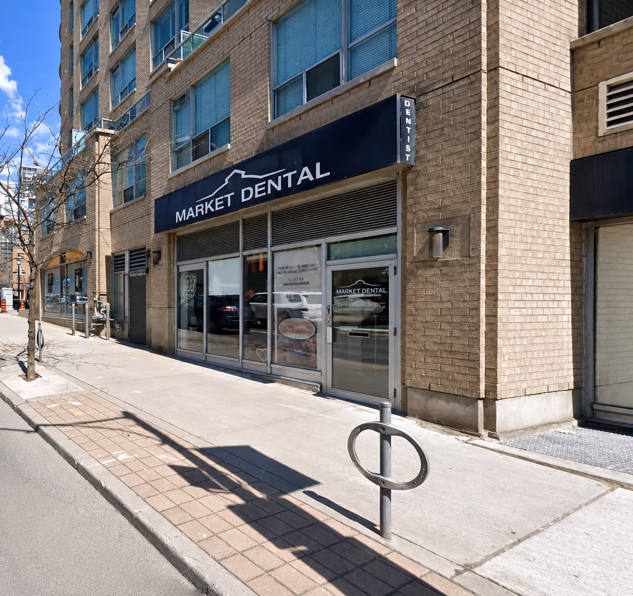 Street view of Market Dental office with beige brick building and glass door on a sunny day.