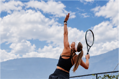 Tenista realizando un saque en una cancha de arcilla al aire libre, con el brazo elevado durante el movimiento.