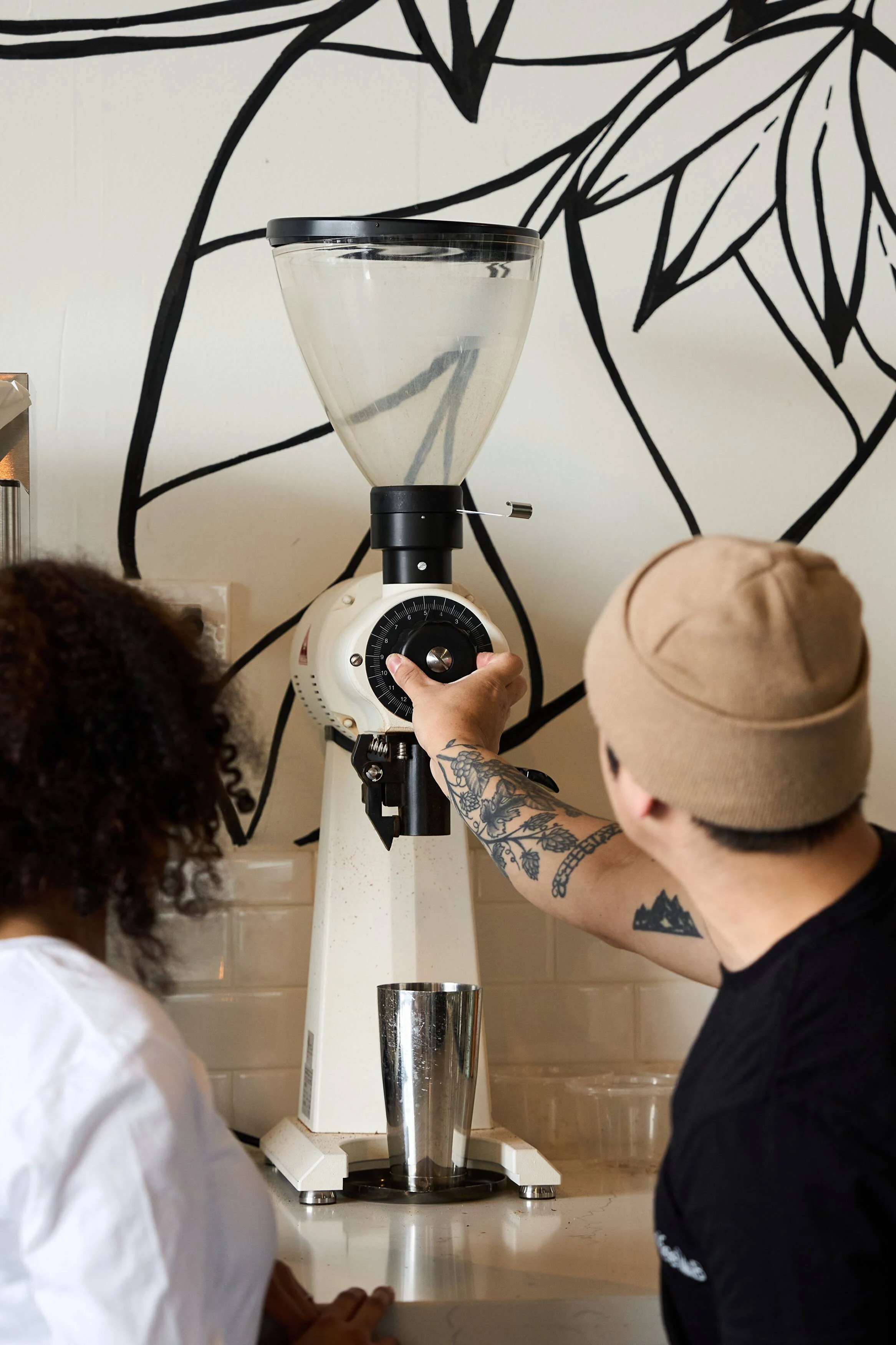 A man in a brown hat is standing next to a coffee grinder.