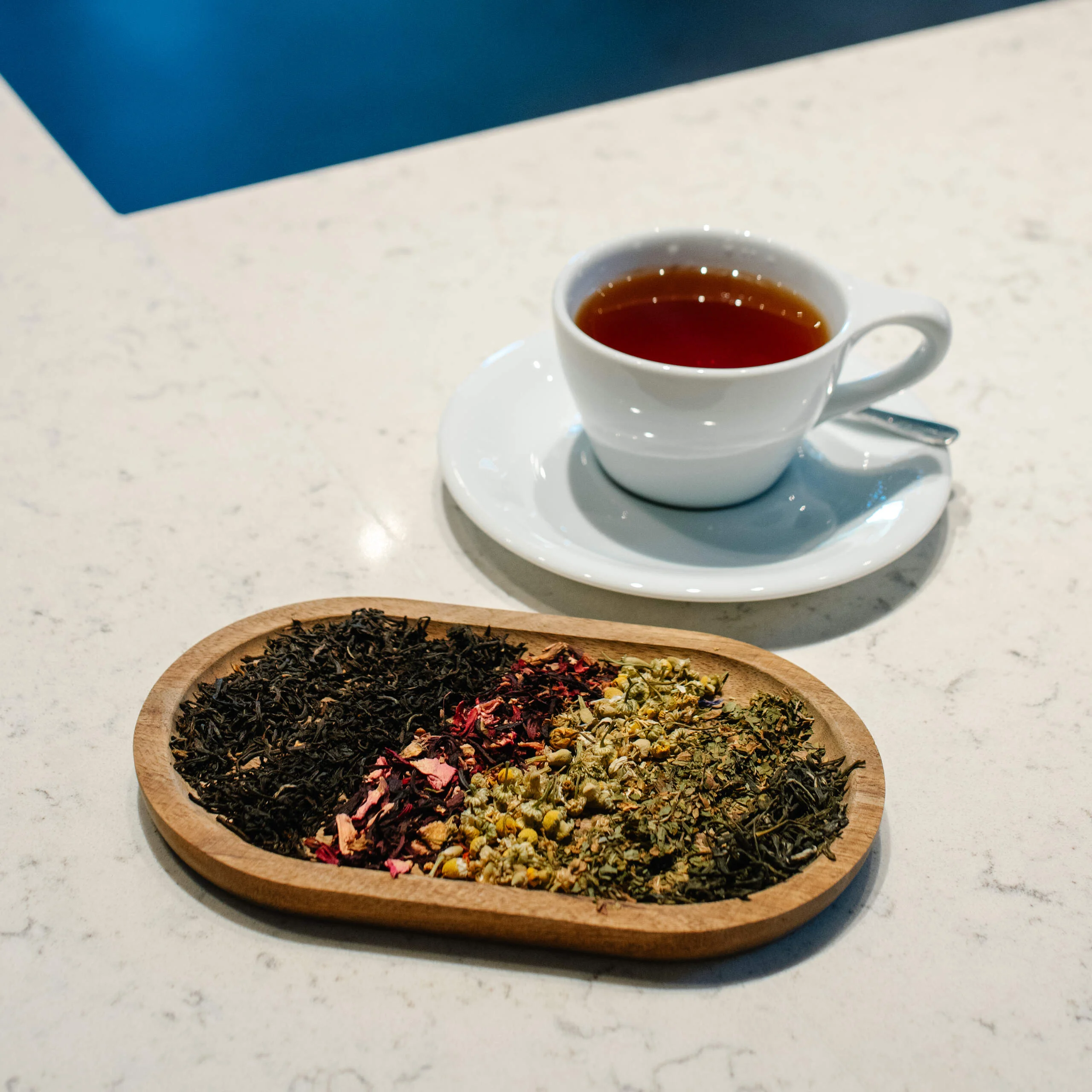 A cup of tea sits on a table next to a wooden tray of tea leaves.