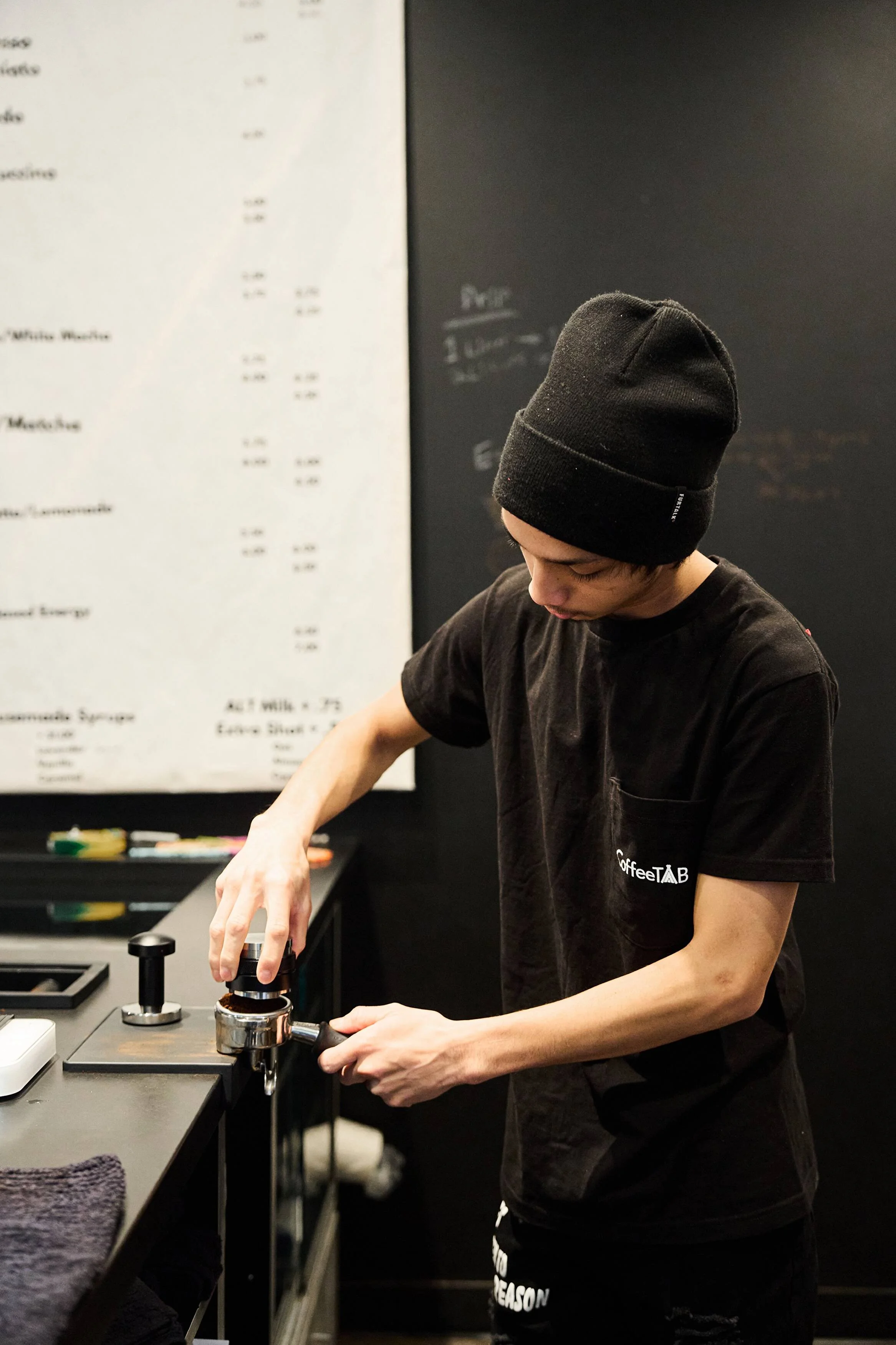 A man wearing a black hat and a black shirt is working on a coffee machine.