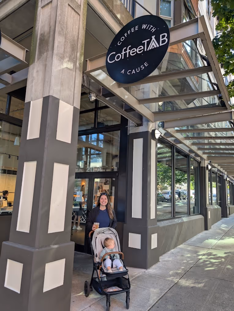 A woman with a baby in a stroller is standing in front of a coffee shop.