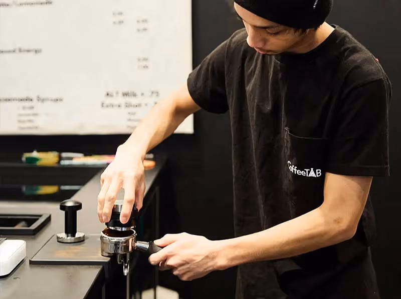 A man wearing a black hat and a black shirt is working on a coffee machine.