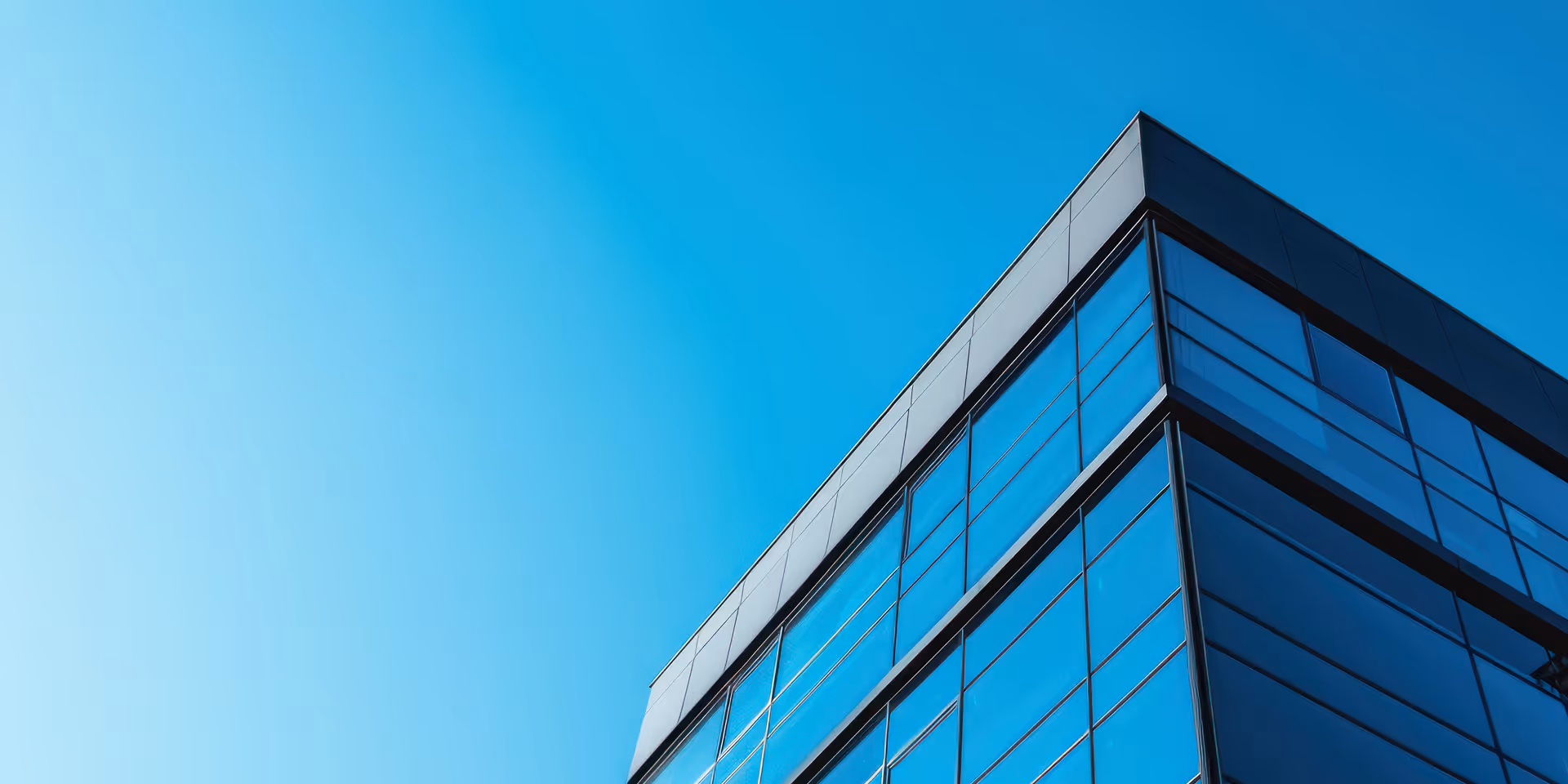 Modern glass building corner reflecting clear blue sky.