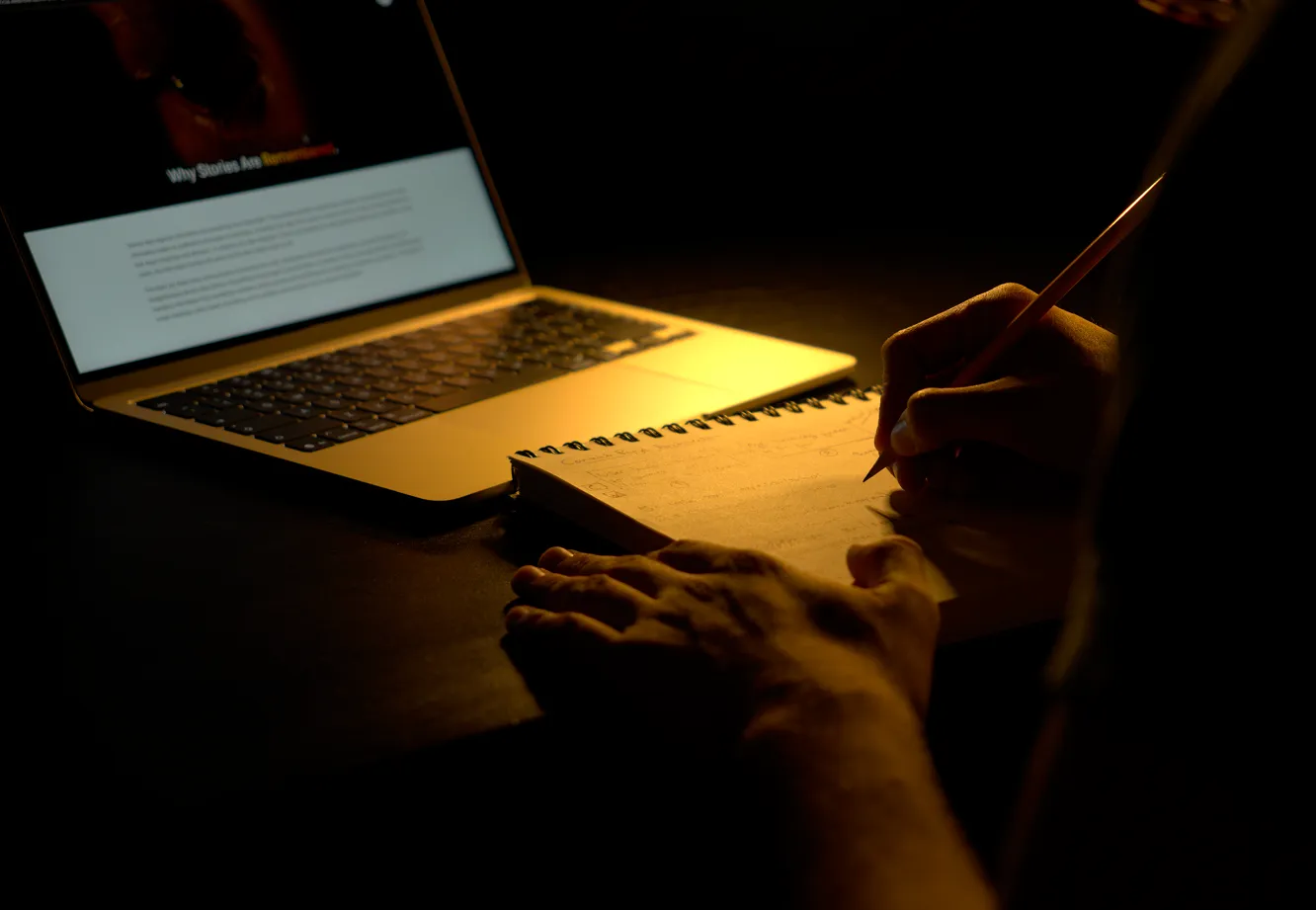 Man studying an article on his laptop while taking notes in his notebook.