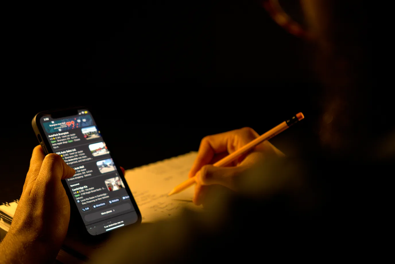 Man reviewing a list of google business profiles on his phone while taking notes.