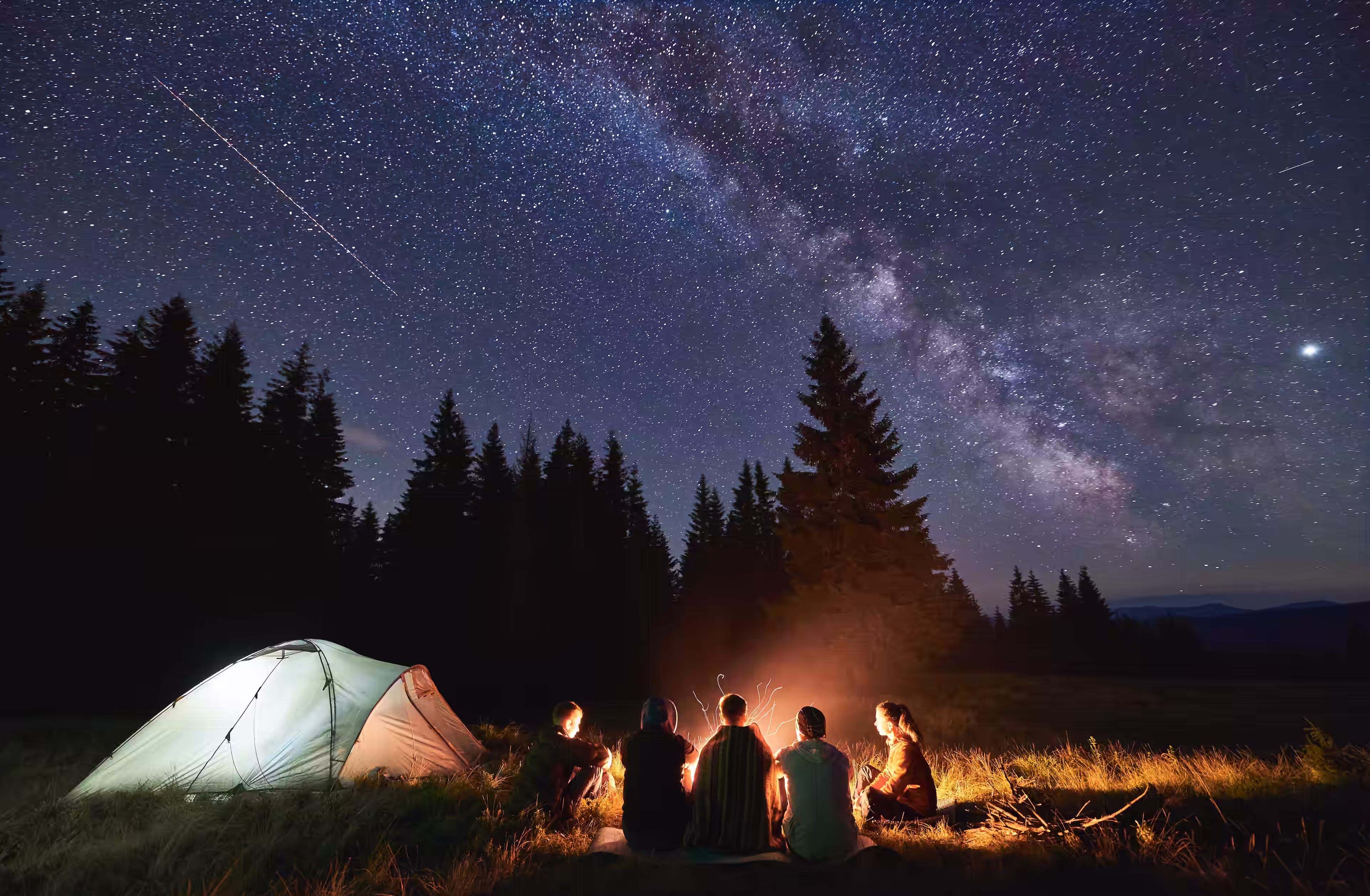 Group of friends sitting around a camp fire on a star filled night