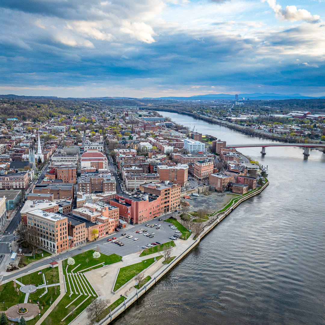 Aerial view of downtown Troy, NY, along the Hudson River with riverfront park and bridge