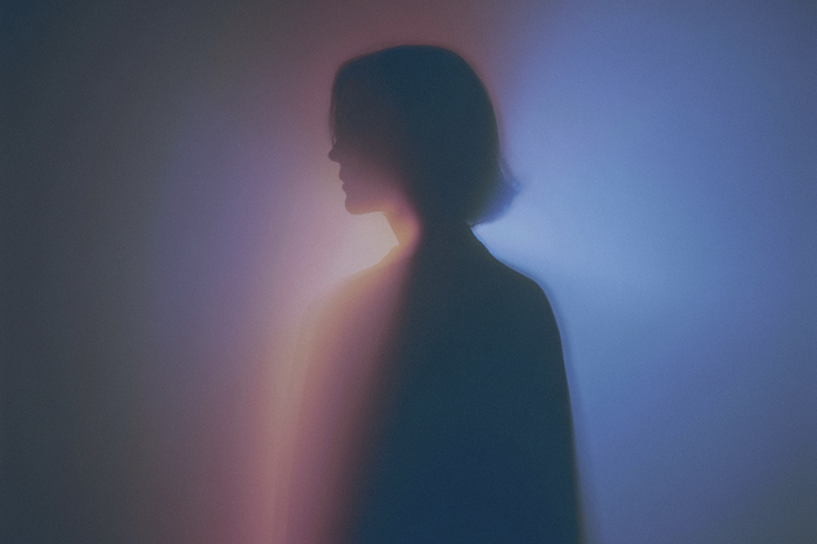 Silhouette of a person with short hair against a soft gradient background of blue and pink light.