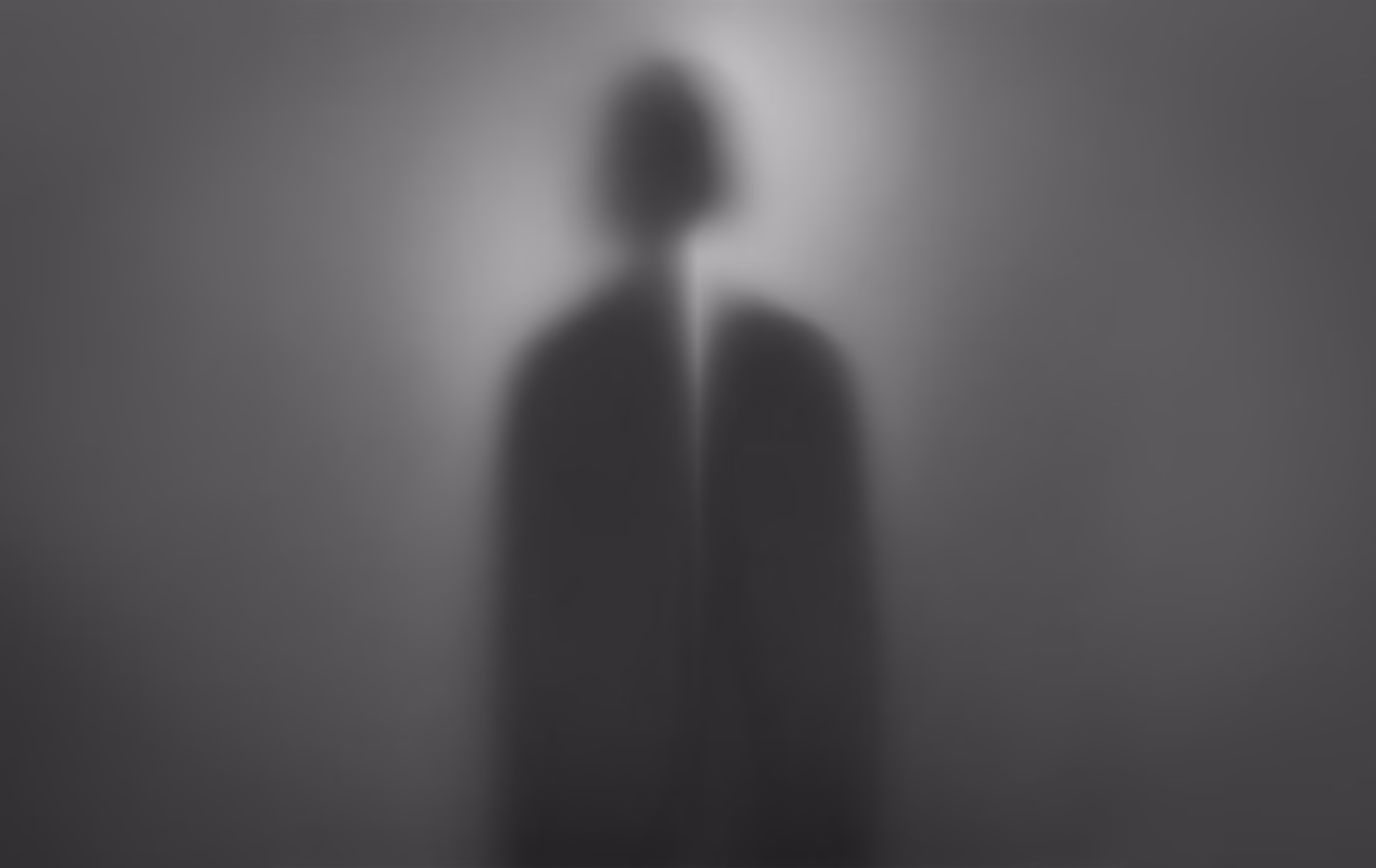 Blurred black-and-white silhouette of a person behind a translucent surface.