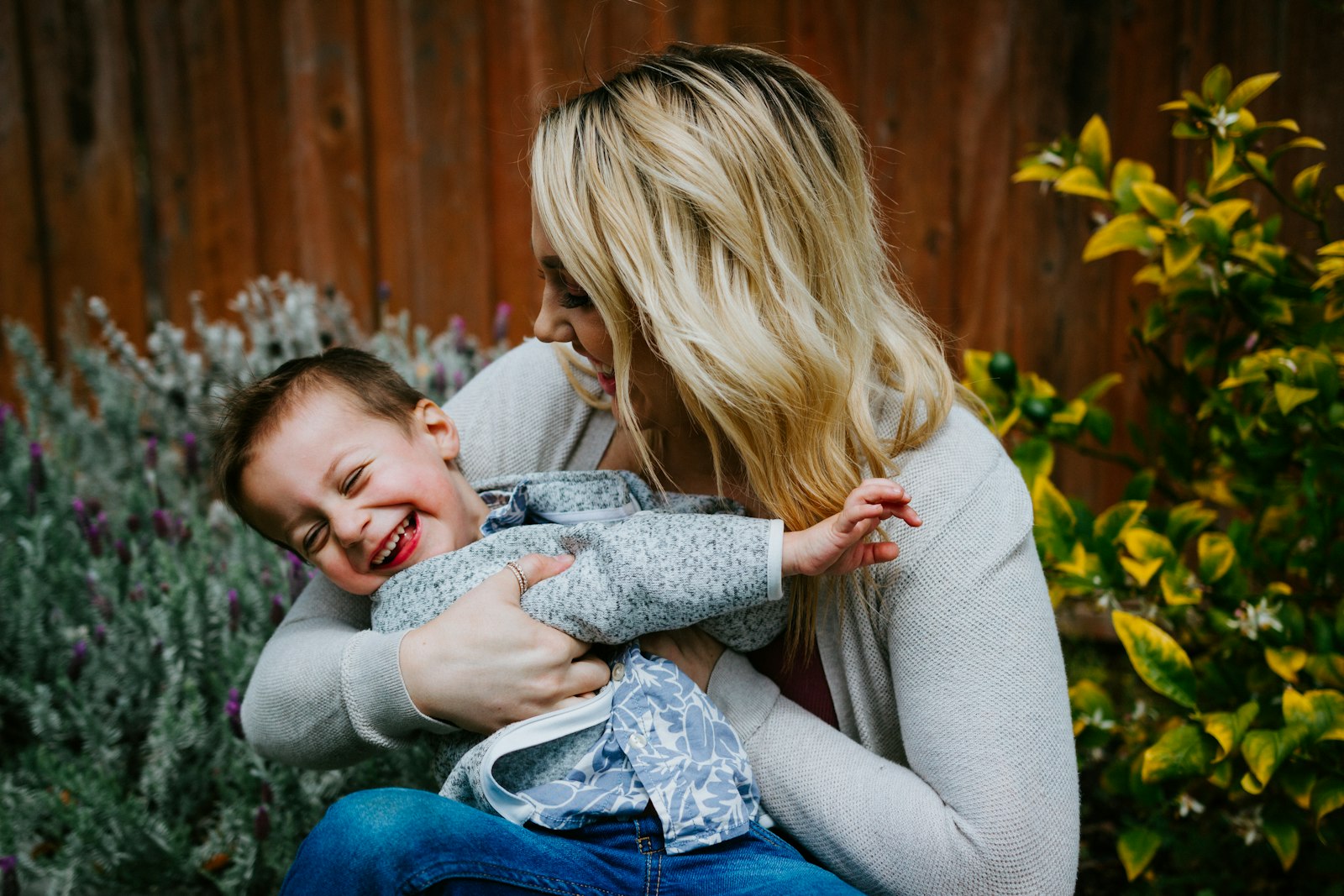 A parent laughing closely with a delighted young child outdoors
